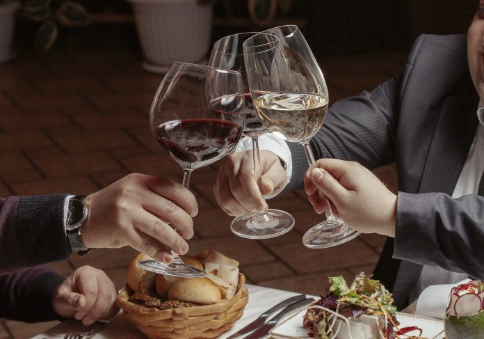 Three friends cheer wine glasses with red and white wine at dinn